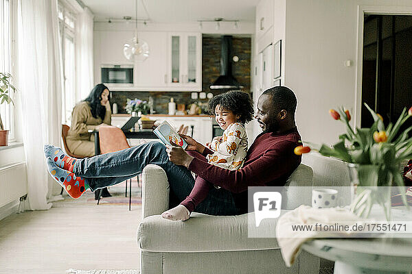 Lächelnder Vater unterrichtet Tochter auf einem Stuhl im Wohnzimmer sitzend
