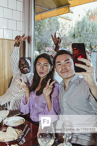 Männliche und weibliche Freunde machen ein Friedenszeichen  während sie ein Selfie mit ihrem Smartphone in einer Bar machen