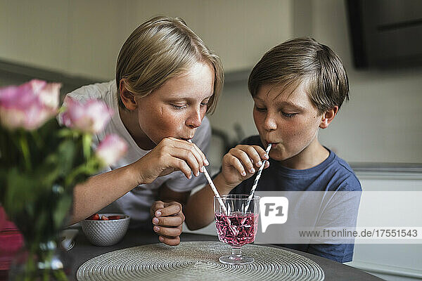 Brothers drinking juice through straw in living room