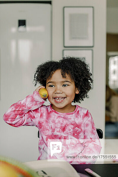 Lächelndes Mädchen hält Banane als Telefon in der Küche zu Hause