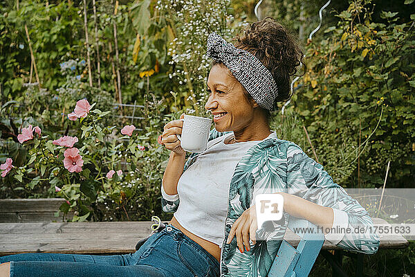 Lächelnde Bäuerin trinkt Kaffee  während sie auf einem städtischen Bauernhof sitzt