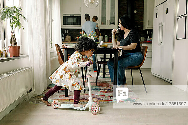 Tochter fährt mit dem Roller  während die Mutter in der Küche arbeitet