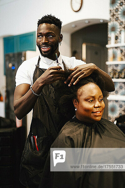 Glücklicher männlicher Friseur  der einer Kundin im Friseursalon die Haare schneidet