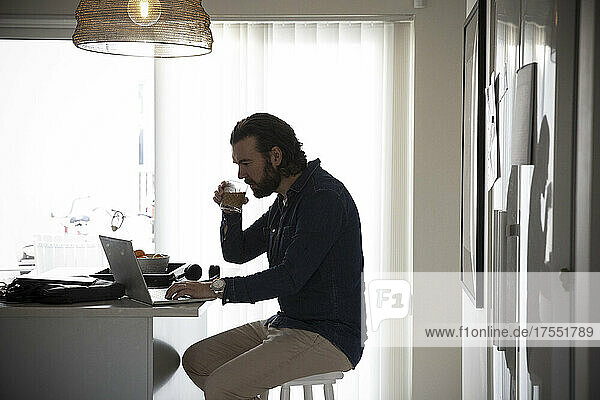 Männlicher Freiberufler trinkt Kaffee bei der Arbeit zu Hause