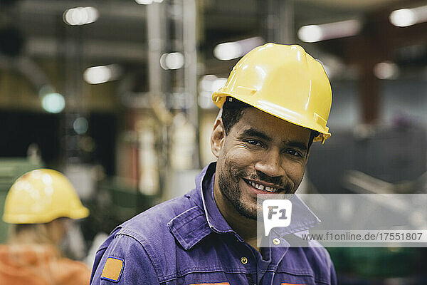 Portrait of confident male blue-collar worker wearing hardhat in factory