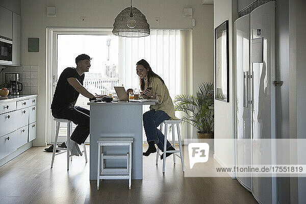 Lächelndes junges Paar benutzt Laptop bei der Arbeit in der Küche