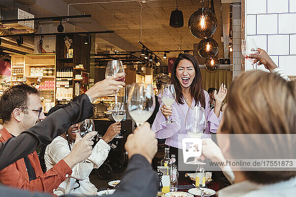 Fröhliche männliche und weibliche Freunde stoßen in einem Restaurant mit Weingläsern an