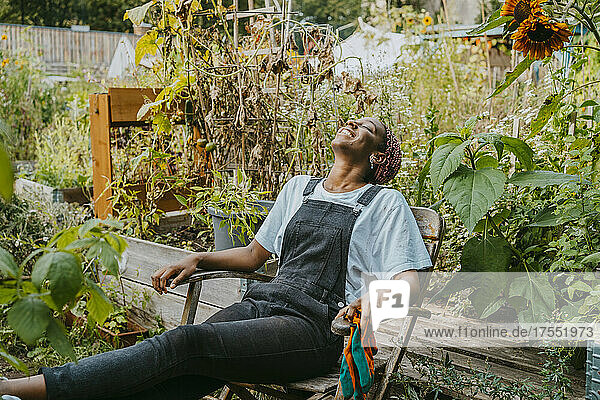 Happy female agricultural shareholder relaxing on chair in urban garden