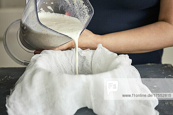Mandelmilch herstellen: Mischung aus gemahlenen Mandeln und Wasser durch Gazetuch abseihen