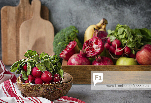 Ein Bund frisches Radieschen in Holzschale  frisches Obst und Gemüse dahinter