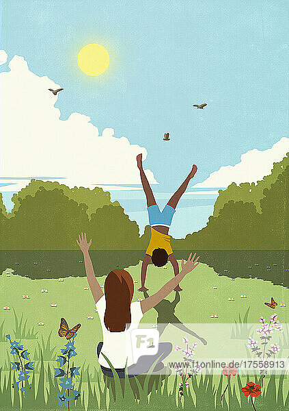 Eine Frau jubelt einem Mann zu  der auf einer sonnigen  idyllischen Frühlingswiese einen Handstand macht