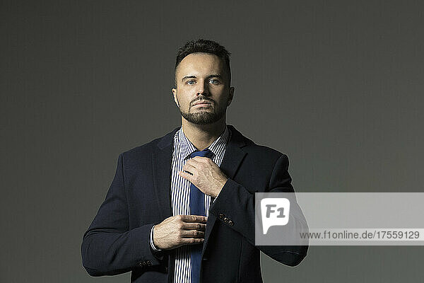 Portrait confident  handsome businessman adjusting necktie against black background