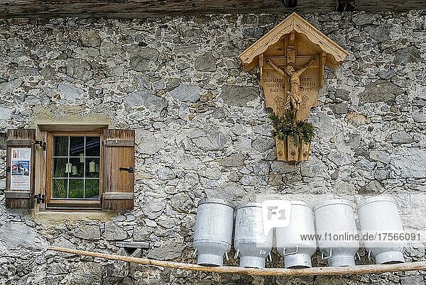 Milchkannen aufgereiht auf einer Holzbank  Fenster und Marterl mit Jesus am Kreuz  Fassade aus groben Steinen einer Alm  Gramaialm  Alpenpark Karwendel  Tirol  Österreich  Europa