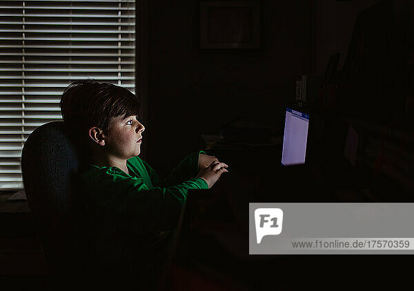 Young boy working on a laptop computer in a dark room.