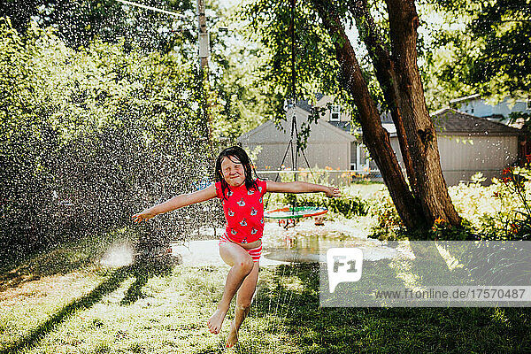 Young girl runs through sprinkler in backyard during summer