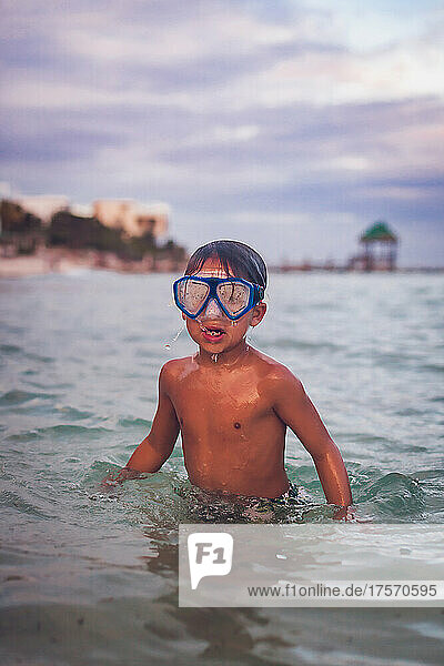 Boy swimming with goggles in the ocean.