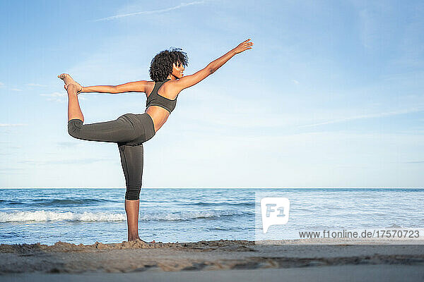 black woman smile doing yoga posture by the sea