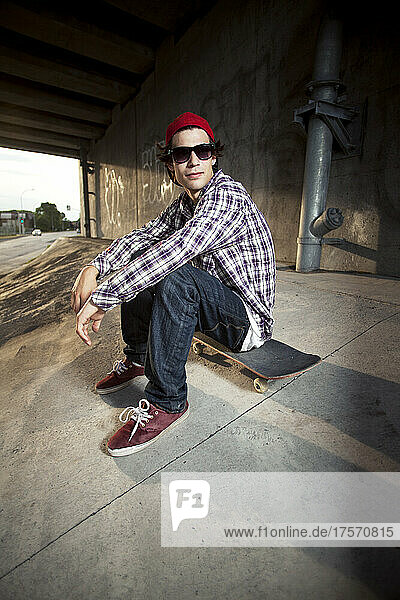 Skateboarder under overpass sitting with sunglasses
