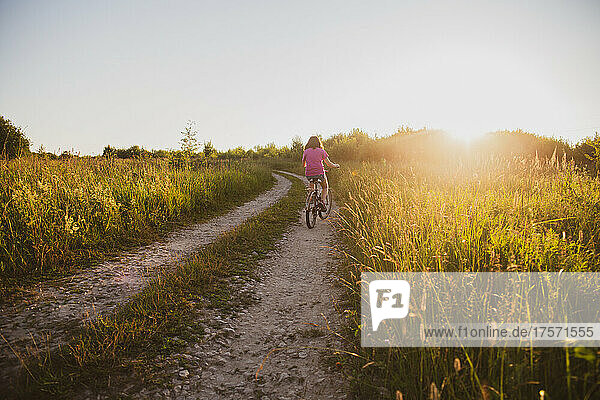 A teenage girl rides a bicycle along a country road in a field