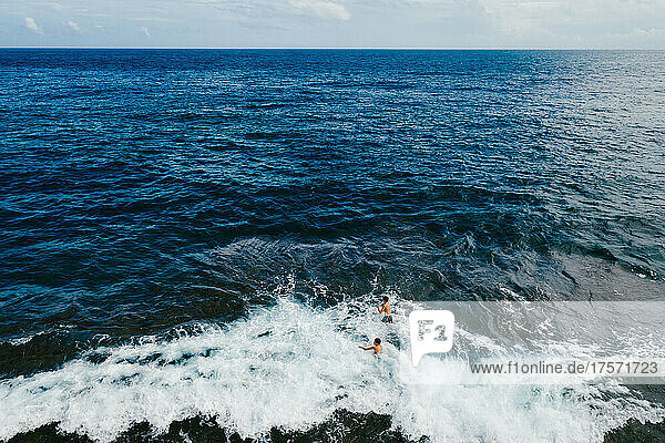 Two boys playing in the waves on the edge of the blue ocean