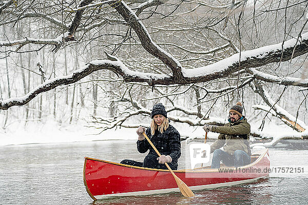 Man and woman paddling a wooden canoe on the snowy river.
