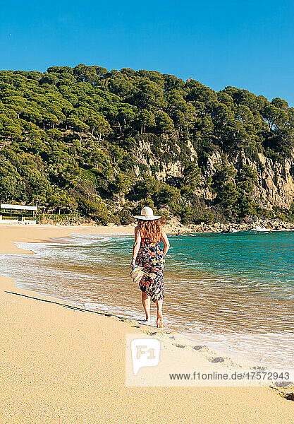 50 year old woman walking with a hat on a beach