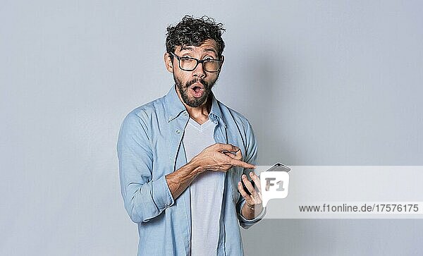 Young man showing blank cell phone screen  concept of shocked man pointing at his cell phone