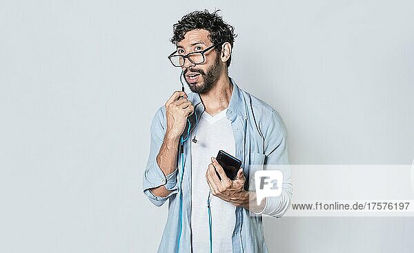 Handsome man talking with headset holding cellphone  young man in glasses with earphones isolated