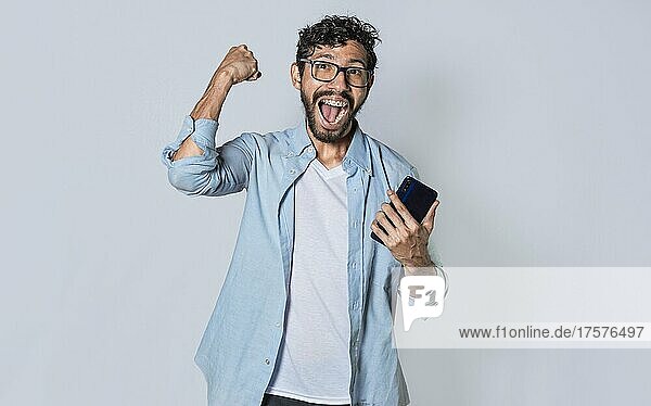 Glücklicher Mann hält ein Smartphone und feiert  aufgeregter Mann schaut auf sein Smartphone