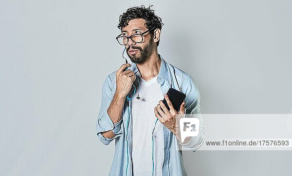 Handsome man talking with headset holding cellphone  young man in glasses with earphones isolated