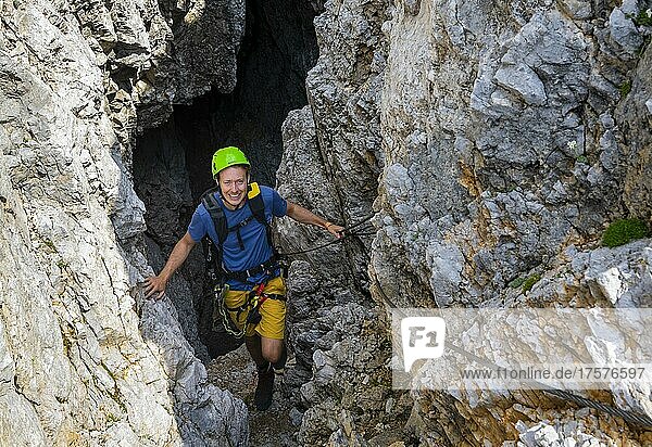Young man climbing out of a rock hole  via ferrata Brudertunnel  Karwendel Mountains  Alpenpark Karwendel  Tyrol  Austria  Europe
