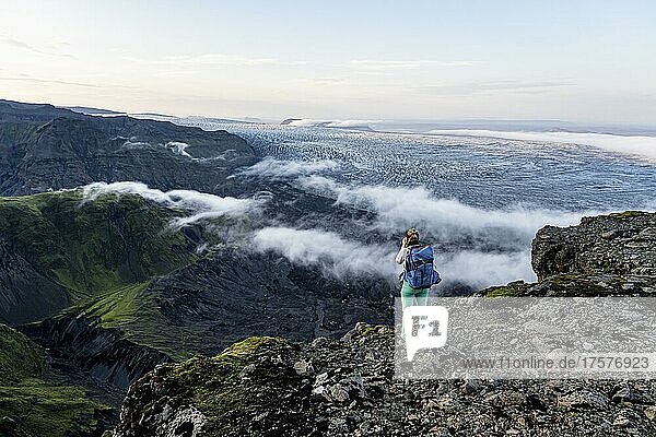 Hiker looks over spectacular landscape  mist on cliffs and glacier Myrdalsjökull  Pakgil  Iceland  Europe