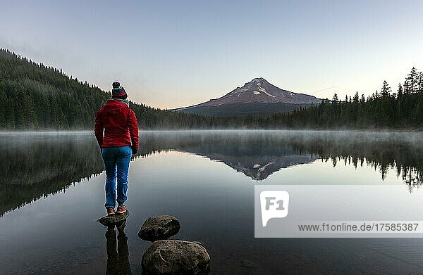 Young woman standing on a stone  reflection of Mt. Hood volcano in Trillium Lake  at sunrise  Oregon  USA  North America
