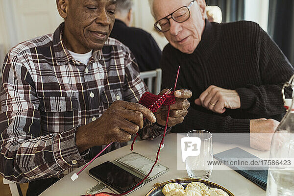 Älterer Mann strickt mit einem männlichen Freund im Altersheim