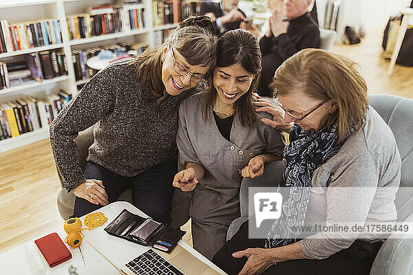 Smiling female nurse teaching laptop to elderly women at retirement home