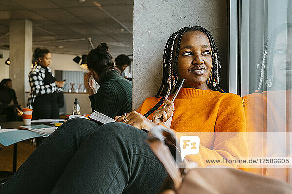Nachdenkliche junge Frau sitzt mit einem Buch in der Universitätscafeteria
