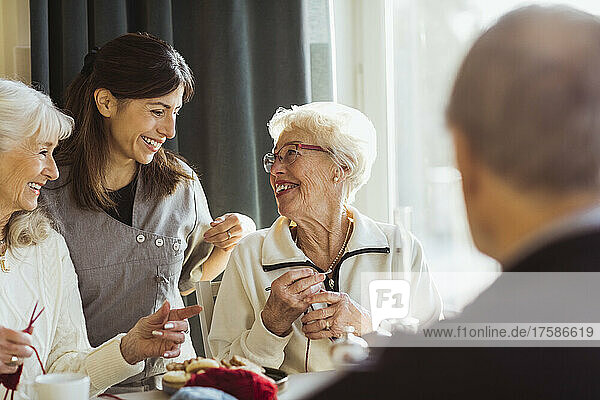 Smiling female healthcare worker talking with senior women knitting in nursing home
