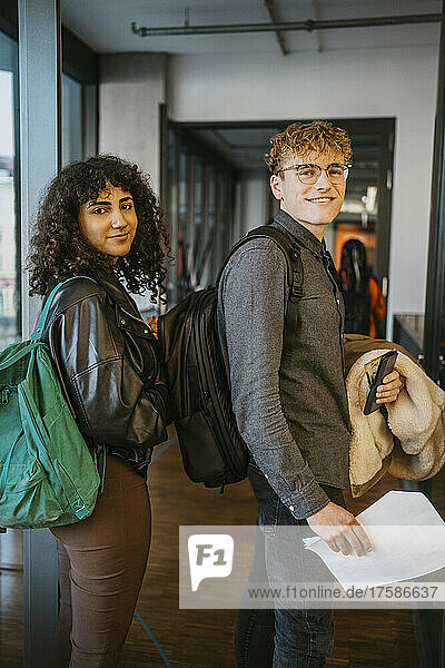 Smiling young male and female students looking back over shoulders in community college