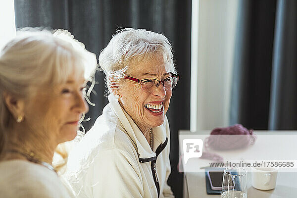Cheerful senior woman sitting by female friend in nursing home