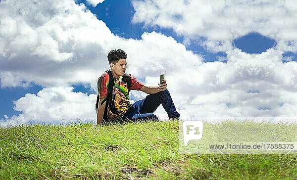 Rucksacktourist mit Telefon auf einer Anhöhe  ein Mann sitzt mit seinem Handy im Gras