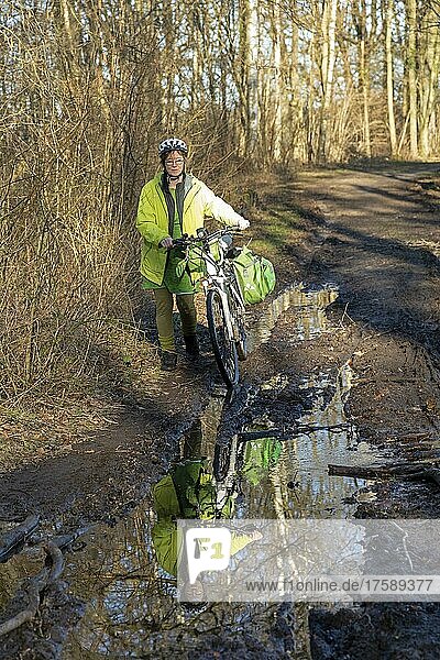 Woman cycling with e-bike over muddy forest path and through puddles  Lüneburg  Lower Saxony  Germany  Europe