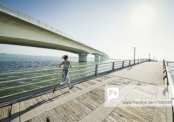 Rear view of woman jogging on bridge on sunny day