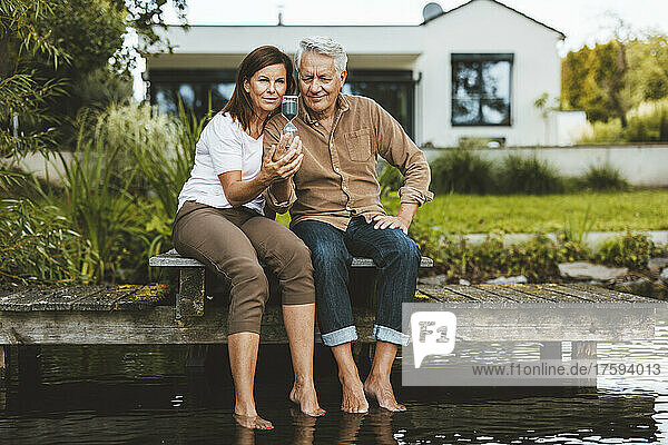 Couple with hourglass sitting on jetty by lake at backyard