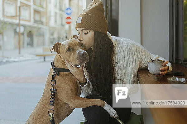 Junge Frau küsst Hund  der im Straßencafé sitzt