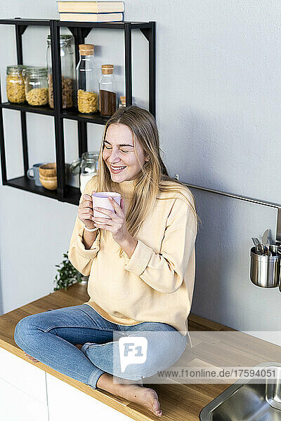 Lächelnde Frau mit Kaffeetasse  die in der Küche träumt