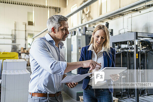 Businessman and businesswoman discussing over tablet PC in factory