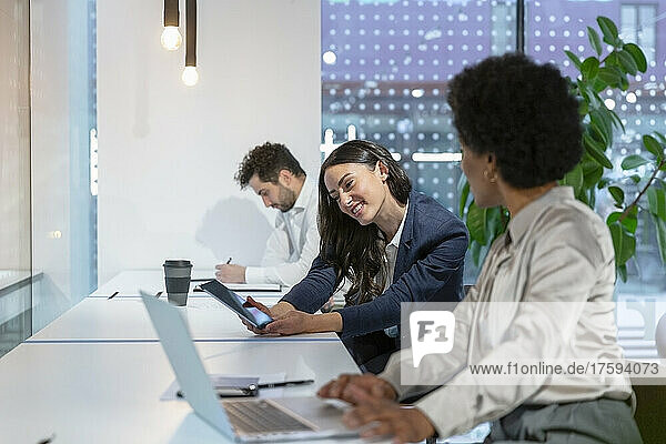 Lächelnde Geschäftsfrau teilt Tablet-PC mit Kollege am Schreibtisch im Büro