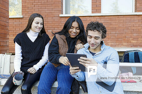 Man sharing tablet PC with friends on university campus