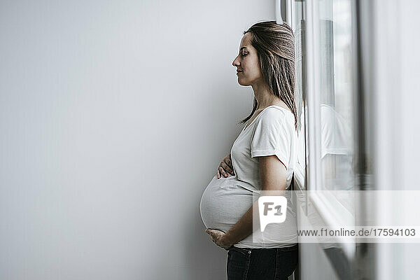 Pregnant woman leaning on window at home