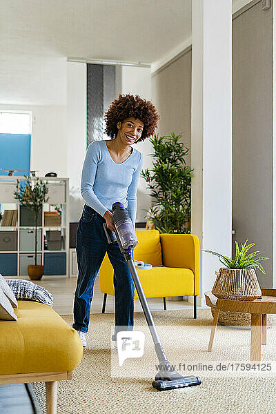 Smiling young Afro woman cleaning carpet in living room at home